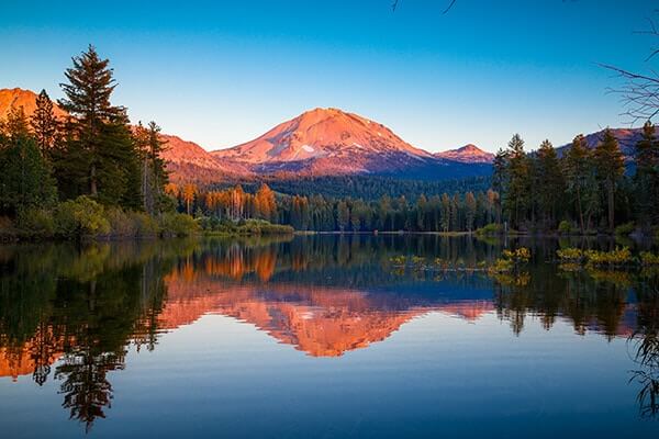 An awe-inspiring image of Lassen Volcanic National Park in California, showcasing the park's unique geological features and stunning natural landscapes. The image captures a volcanic peak, its rugged and jagged silhouette rising against the backdrop of a clear blue sky.