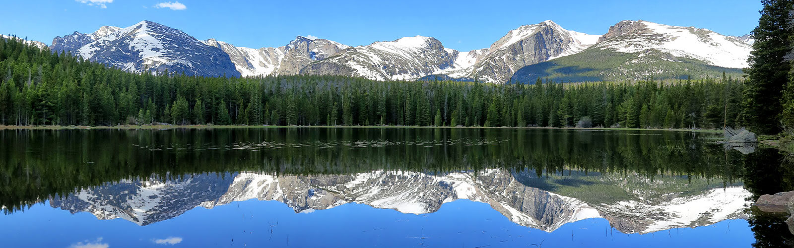 RV parked at a scenic Colorado campground with snow-capped mountains and a lake in the background.