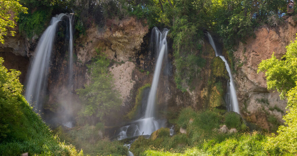 Rifle Falls State Park campground with triple waterfall and lush greenery in the background.