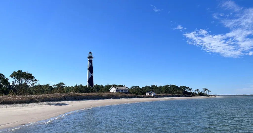 In the distance, the iconic Cape Lookout Lighthouse stands tall, its white stripes contrasting against the blue sky. Cape Lookout National Seashore is a protected area known for its pristine beaches, abundant wildlife, and rich maritime history.