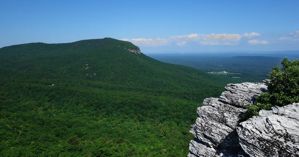 Towering above the landscape is the iconic Hanging Rock, a massive rock formation jutting out into the sky. The rock face is stunning, displaying intricate patterns and textures. Lush vegetation surrounds the area, adding to the park's natural allure.