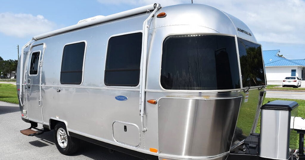 Airstream Sport parked in a scenic campsite, surrounded by trees and nature, with chairs set up outside for relaxation.