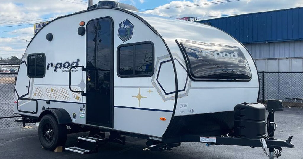 The camper features a slide-out awning, open door, and chairs set up outside for lounging.
