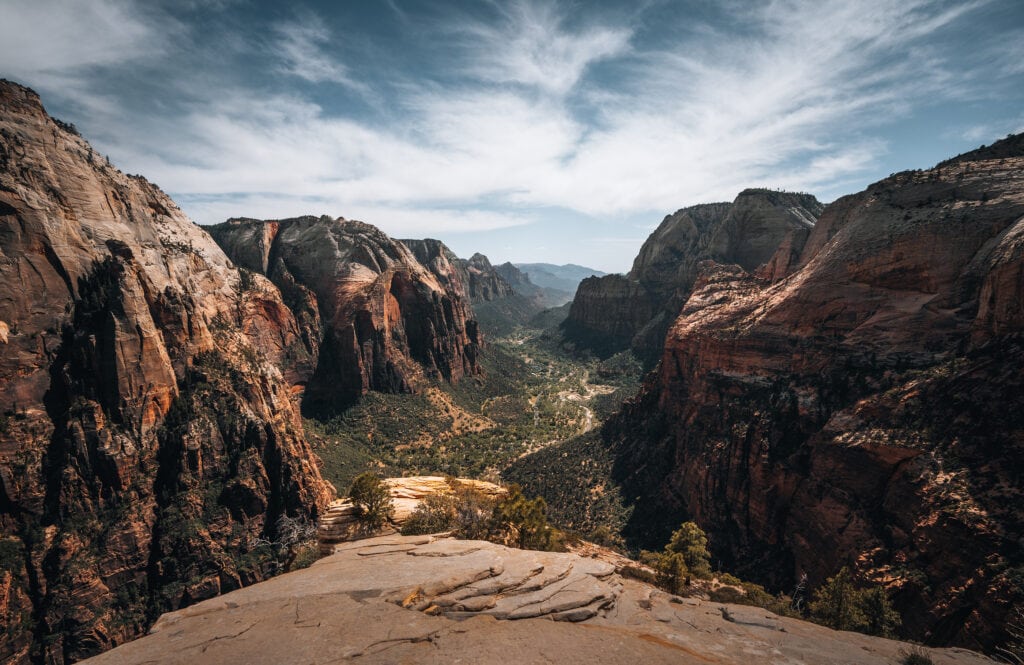 A breathtaking view of Zion Canyon in Utah. Towering red rock cliffs surround a winding river, with lush vegetation dotting the landscape.