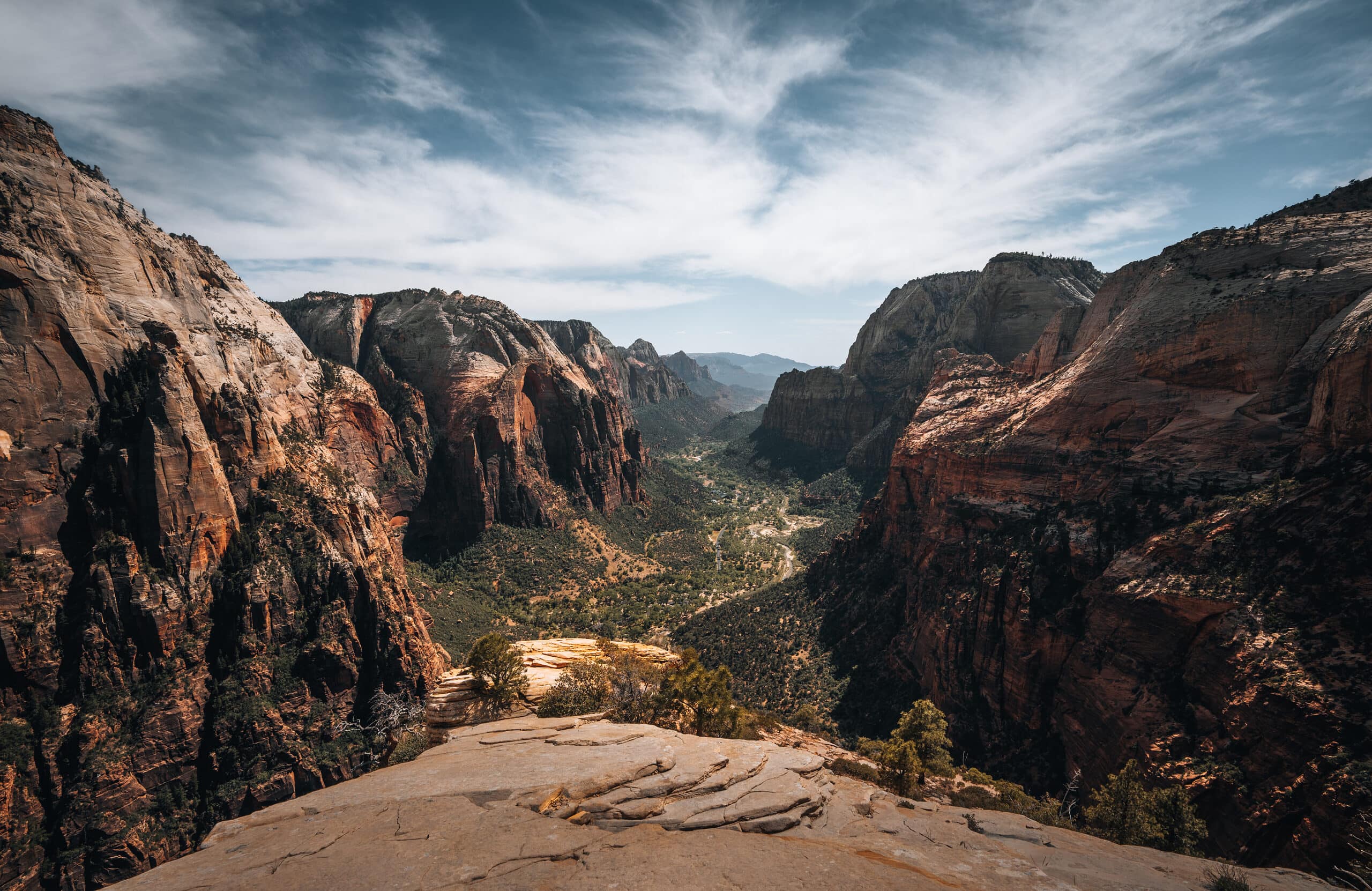 A breathtaking view of Zion Canyon in Utah. Towering red rock cliffs surround a winding river, with lush vegetation dotting the landscape. The clear blue skies add an extra touch of beauty to the scene. Zion Canyon is known for its stunning natural beauty, popular hiking trails, and unique rock formations such as the famous Angel's Landing and The Narrows.