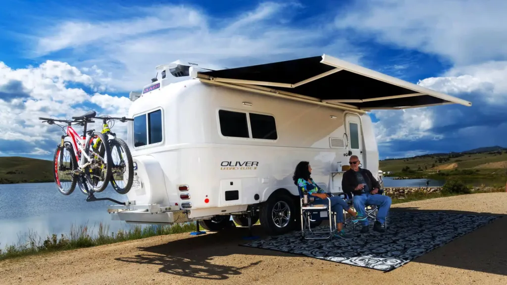The image showcases a sleek and stylish Travel Trailer, widely regarded as one of the best campers in the industry. The camper is parked in a picturesque camping site surrounded by lush greenery and a tranquil lake.