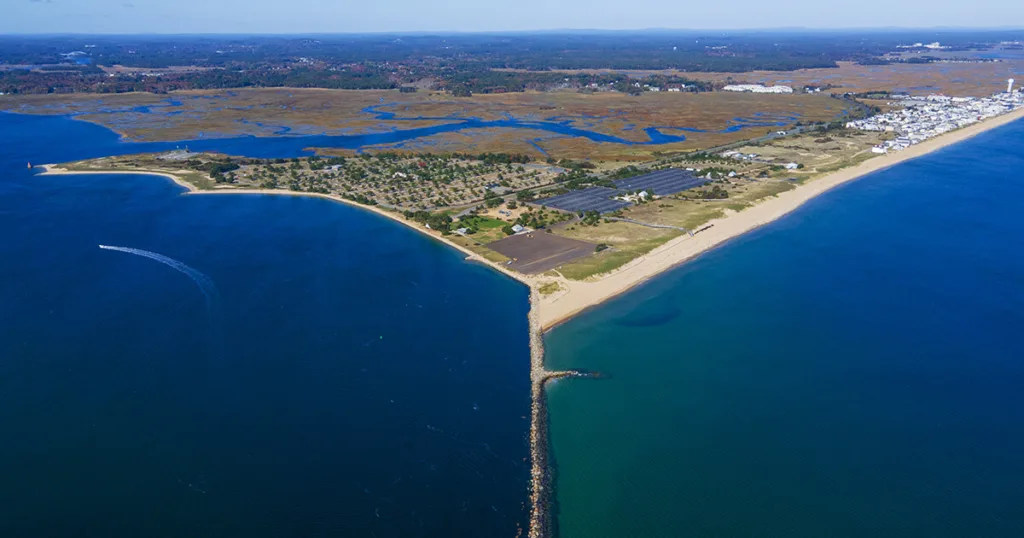 A sunny beach scene at Salisbury Beach State Reservation, with soft golden sand stretching out towards the crystal-clear ocean. People enjoy various activities like swimming, sunbathing, and building sandcastles.