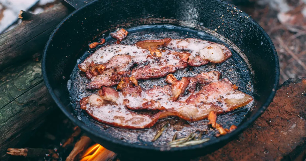 cooking bacon on an open flame campfire