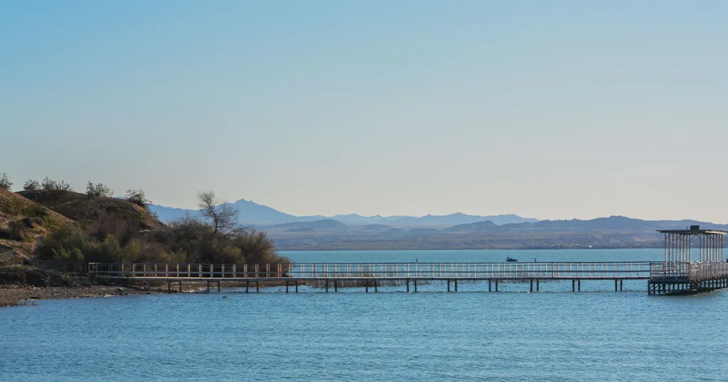 Lake Havasu State Park - picturesque view of the crystal-clear lake surrounded by sandy beaches, palm trees, and rocky desert terrain, providing a tranquil escape for water activities and outdoor adventures in this scenic park located in western Arizona.