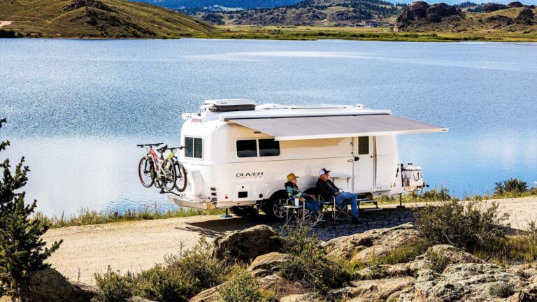 A man and woman with their camper near a lake. This couple is relaxing and enjoying the scenery and nature