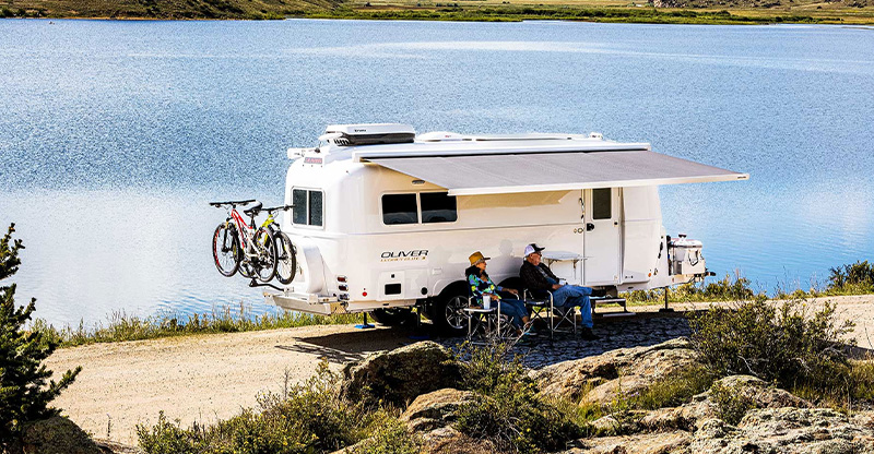 2 couples enjoying being outside camping near a lake with their oliver travel trailer