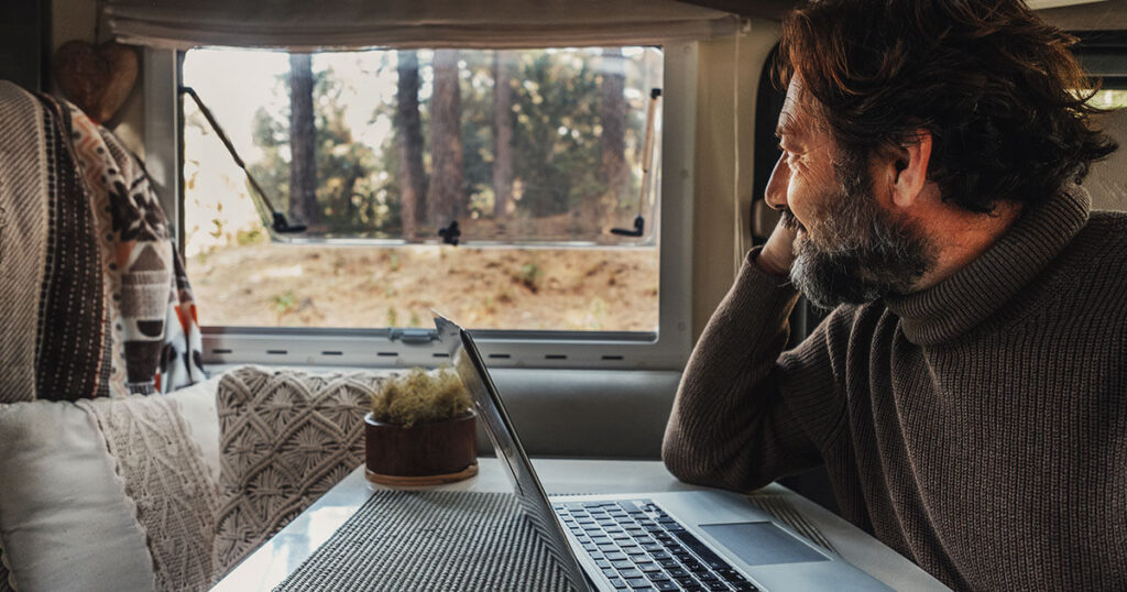 a man on his laptop enjoying coffee while looking out of his RV window