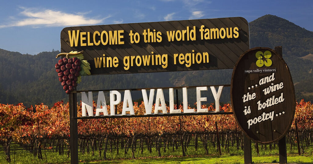 Napa Valley, California: Rolling hills of lush vineyards under a clear blue sky, with a charming winery nestled in the distance.