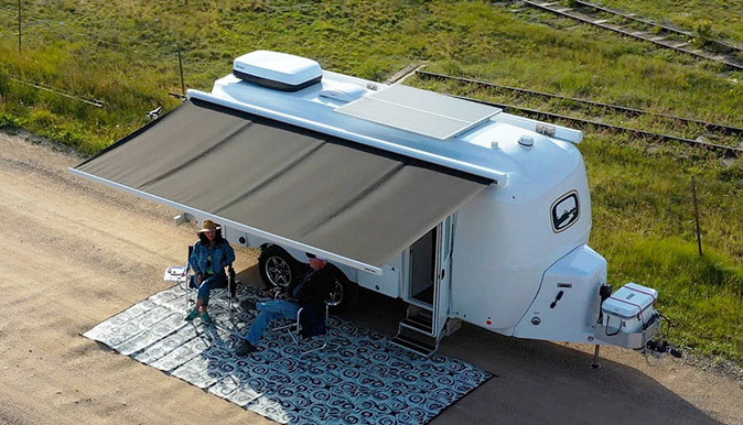 Oliver Travel Trailer in a remote, scenic landscape, featuring solar panels on its roof and a cozy interior with lithium battery tech, embodying adventure and efficiency
