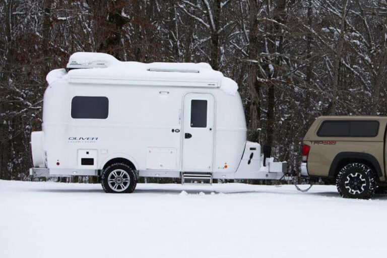 Small camper trailer parked in snow, showcasing its four-season readiness.