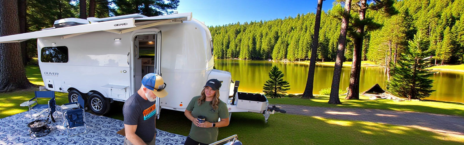 A sleek, silver Oliver Travel Trailer parked on a scenic outdoor landscape, featuring a forested background with tall pine trees and a sunset sky, highlighting its luxurious fiberglass design and premium features, compared to similar Airstream and Bowlus RVs.